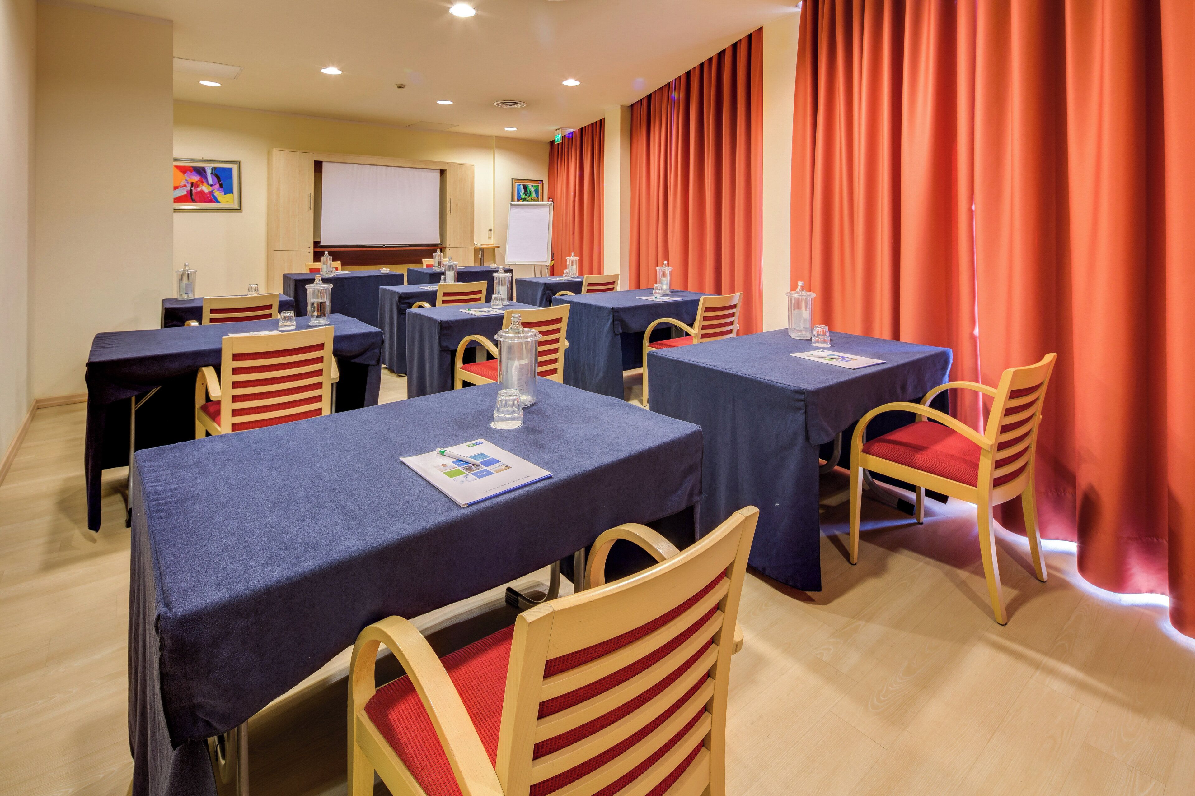 A conference room with tables, chairs, and a projection screen.