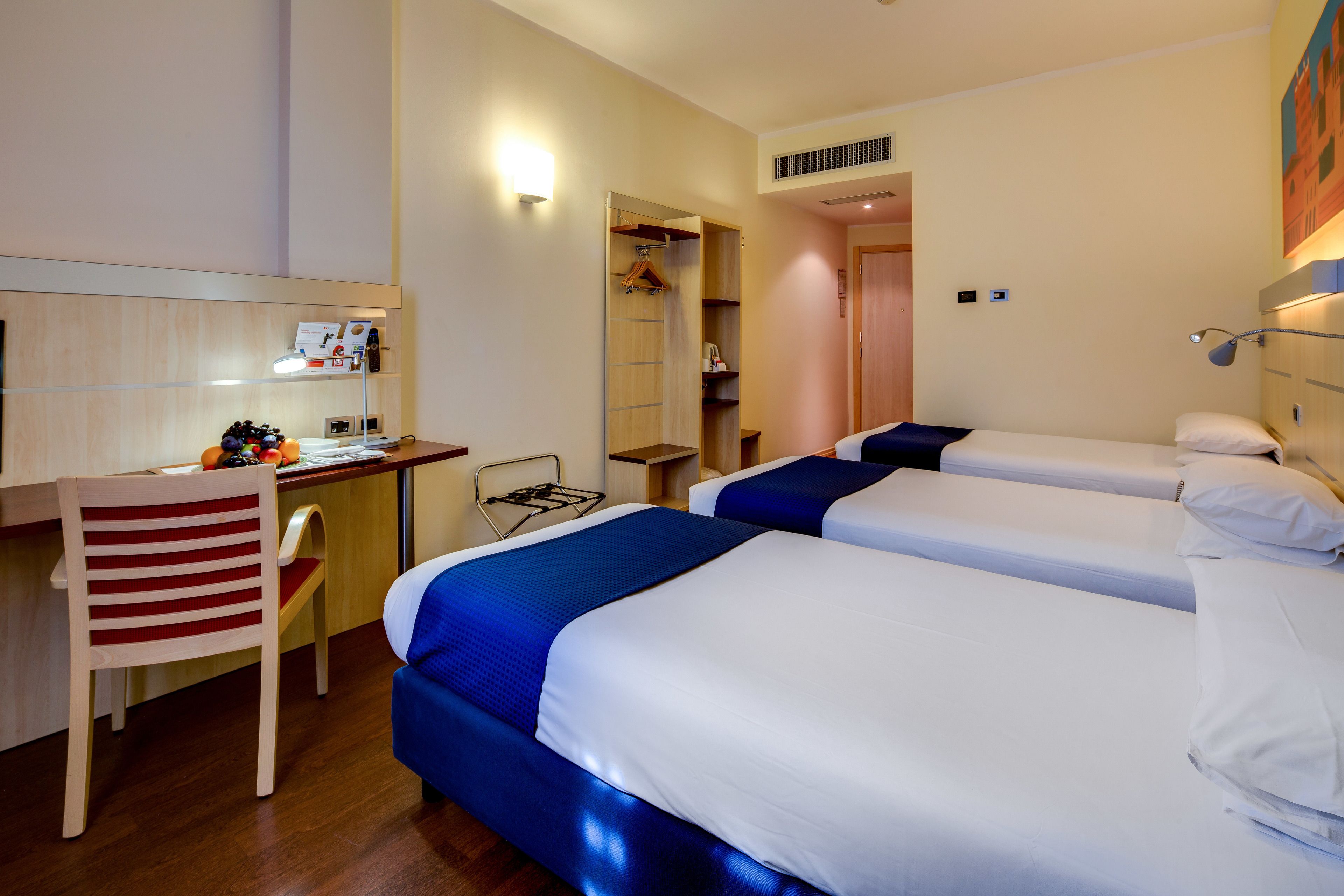 Une chambre d’hôtel avec deux lits, un bureau, une chaise et une armoire.