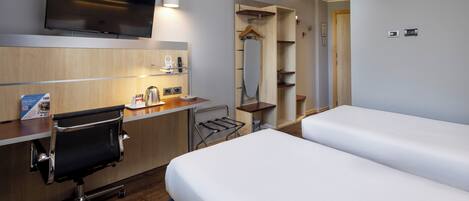A hotel room with a desk, chair, two beds, a TV, and a wardrobe.