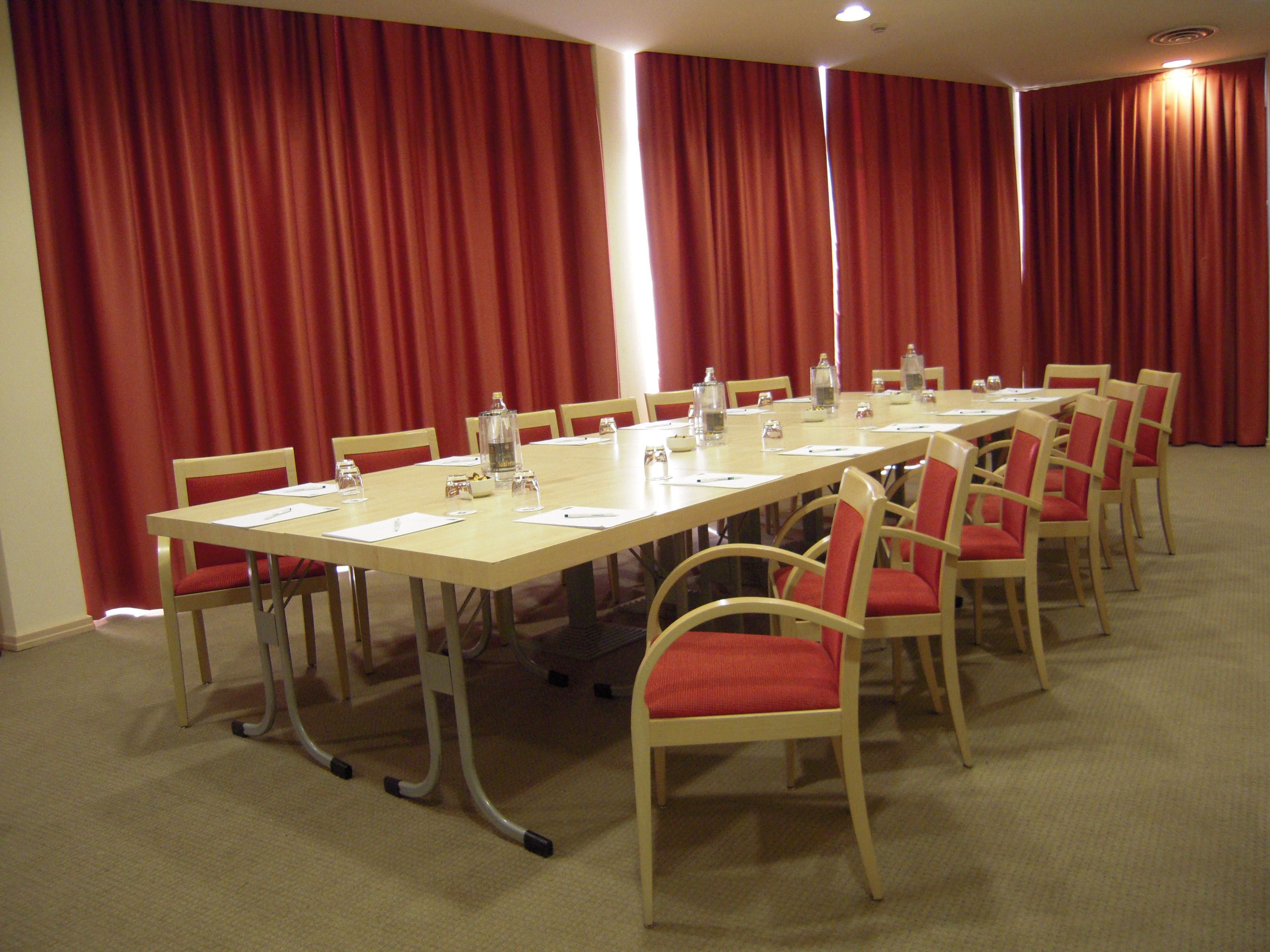 Ein Konferenzraum mit einem langen Tisch, Stühlen und roten Vorhängen.
