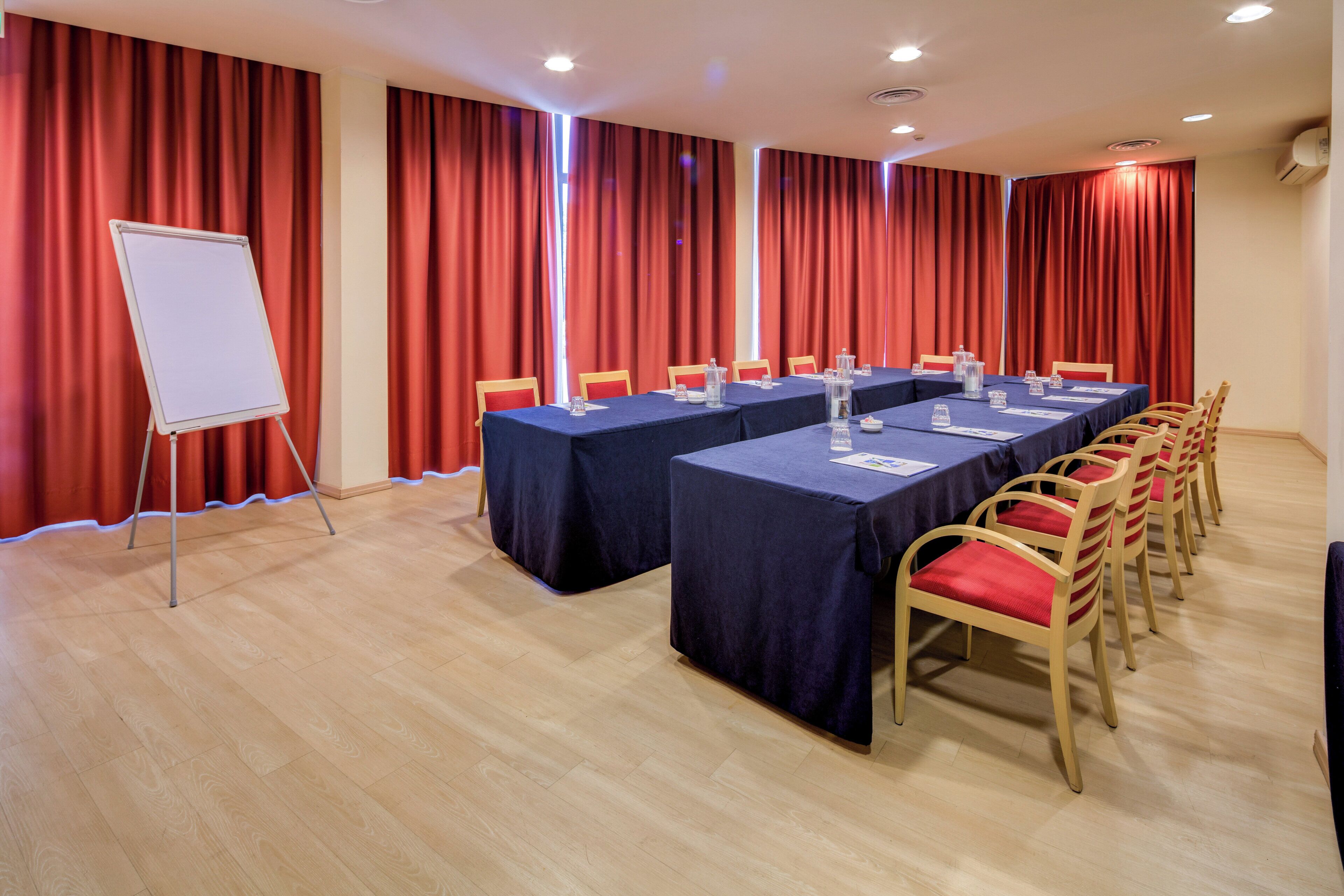 A conference room with a long table, chairs, a whiteboard, and red curtains.