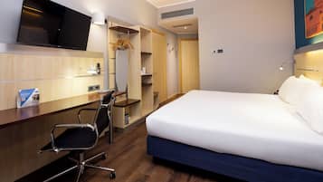 Habitación de hotel con cama, escritorio, silla, televisor, armario y un cuadro en la pared.