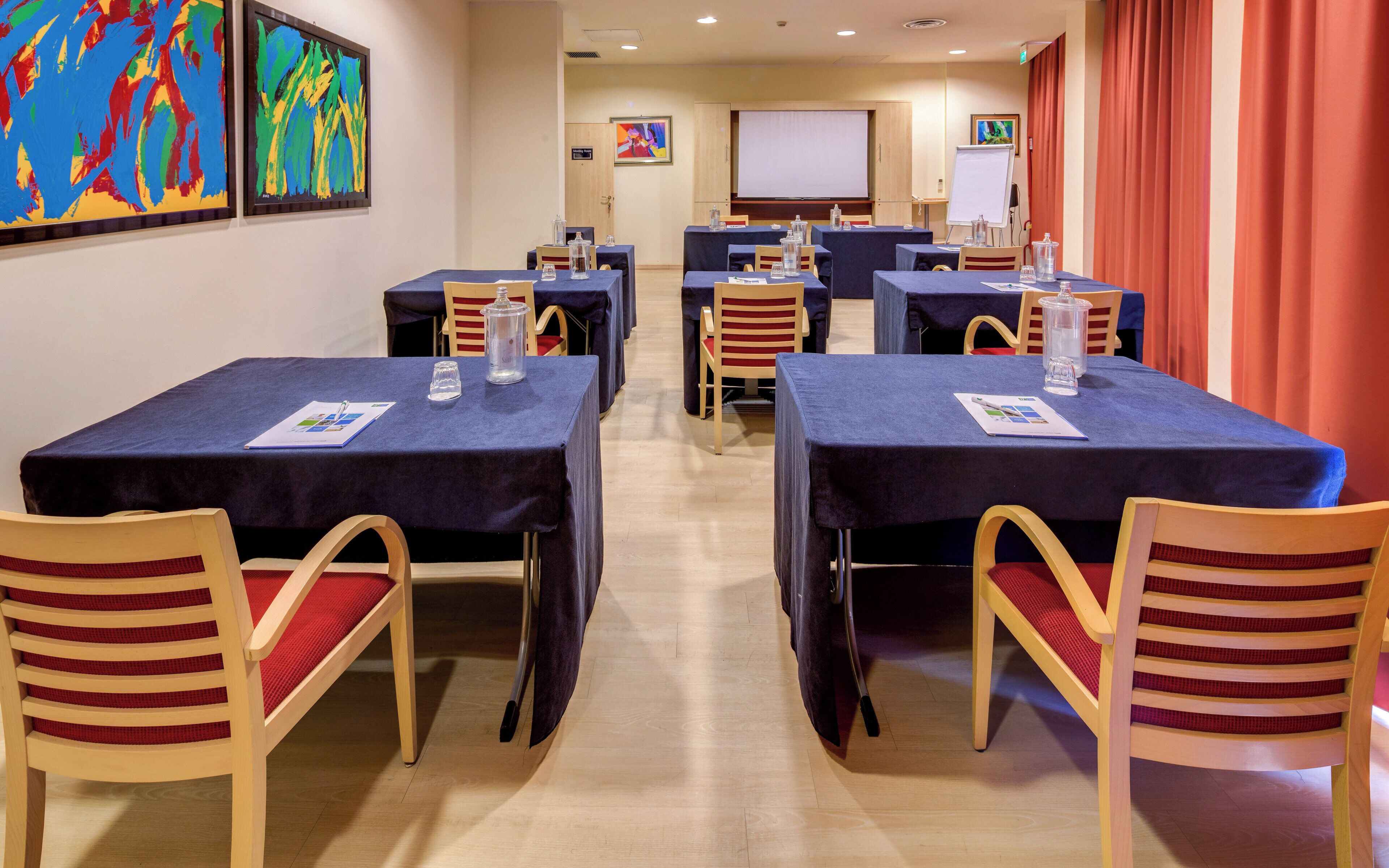 A conference room with tables, chairs, and a projector screen.