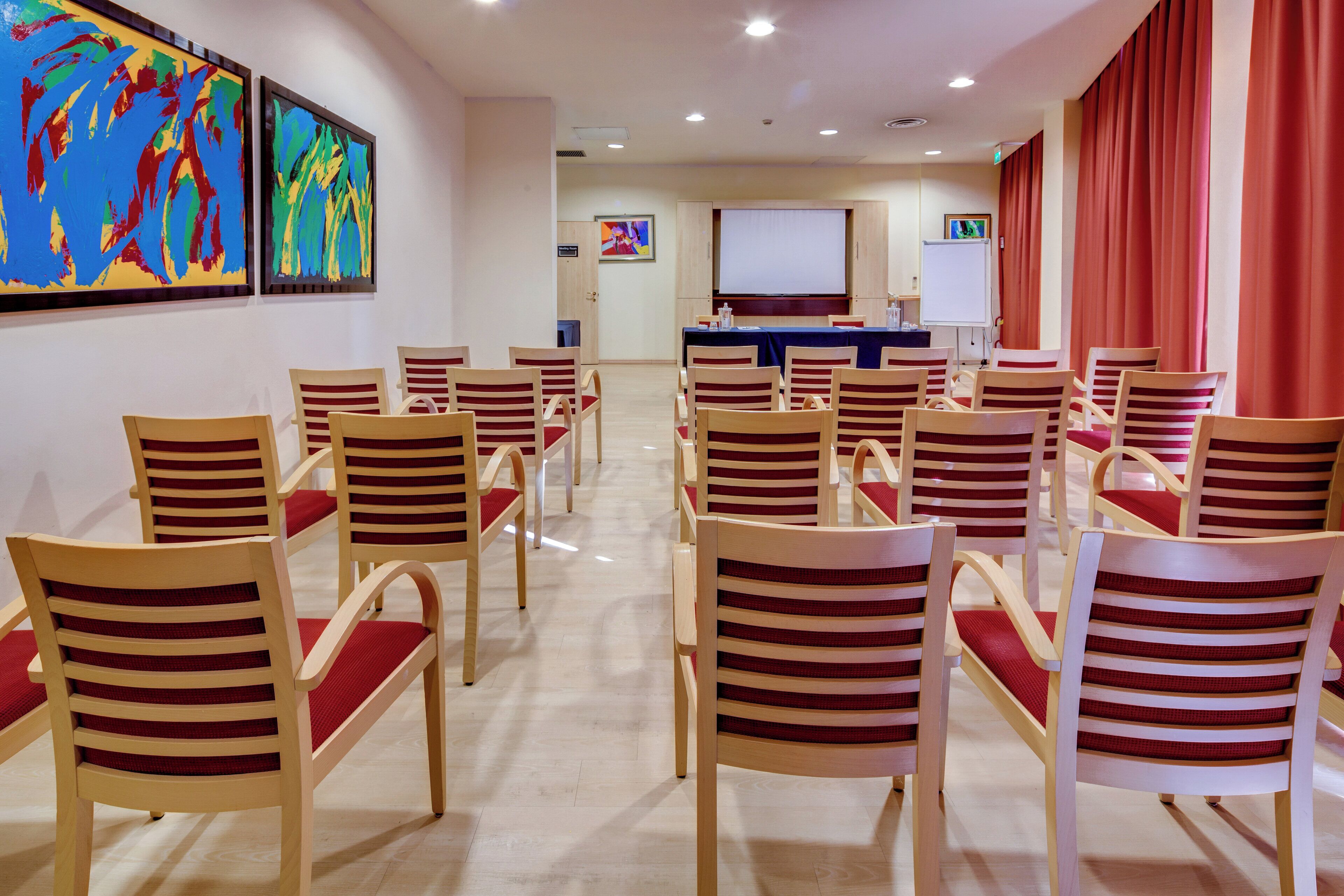 Un salón de conferencias con filas de sillas de madera y una pantalla grande al frente.