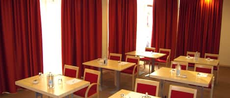 Un salón de conferencias con varias mesas y sillas, cortinas rojas y un ventanal luminoso.