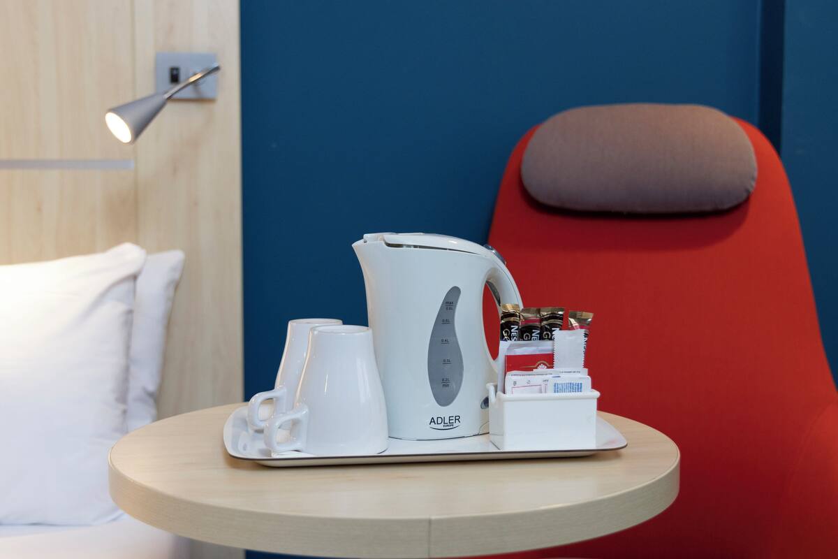 A hotel room with a bed, a red armchair, a small round table with a coffee maker, cups, and a tissue box.