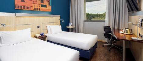A hotel room with two beds, a desk, a chair, a TV, a window with curtains, and a painting on the wall.