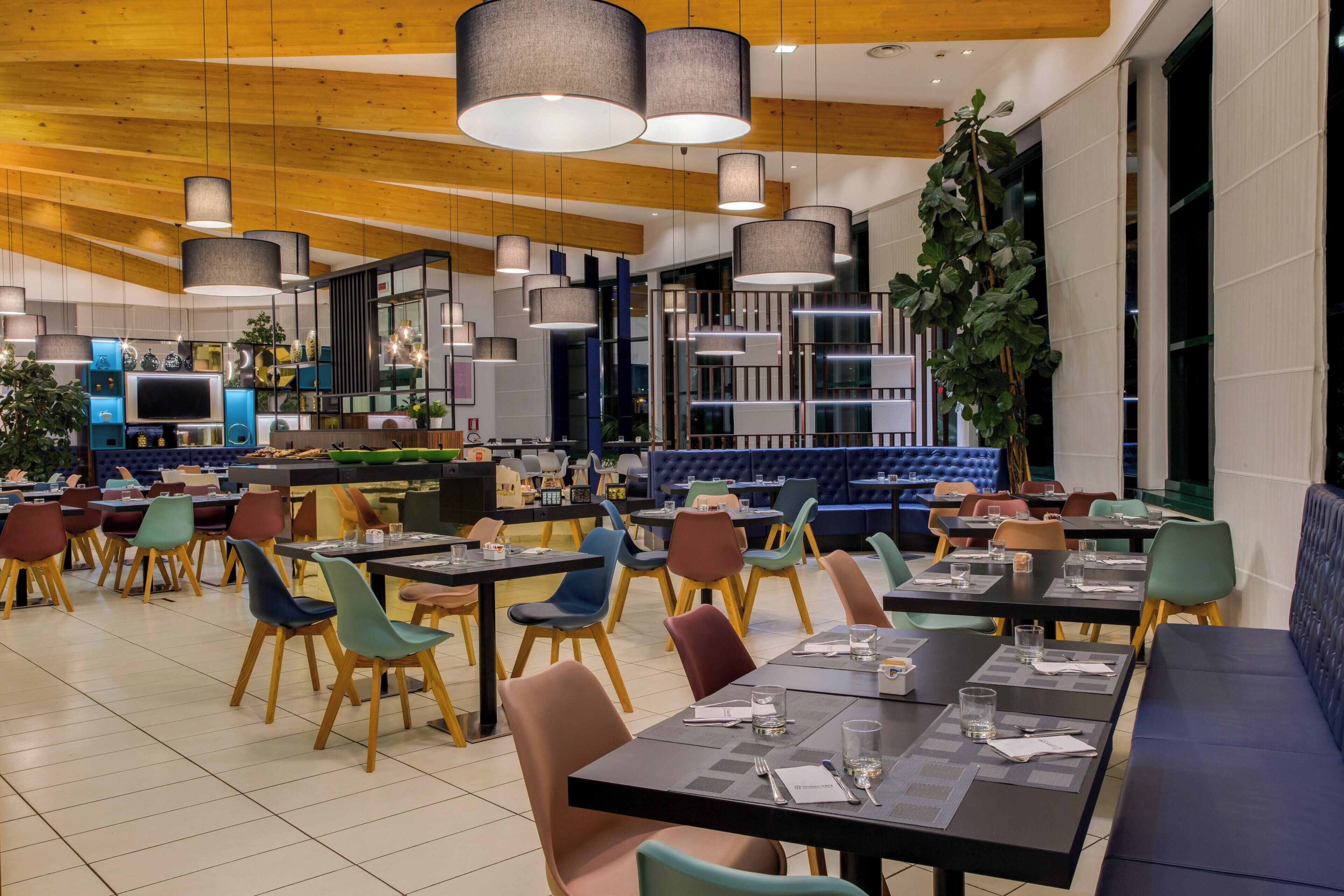 Un interior de restaurante moderno con varias zonas de comedor, techo de madera y luminarias contemporáneas.