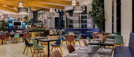 Un interior de restaurante moderno con varias zonas de comedor, techo de madera y luminarias contemporáneas.