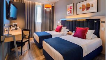 Une chambre d’hôtel avec deux lits, un bureau, une chaise, une télévision et des œuvres d’art accrochées au mur.