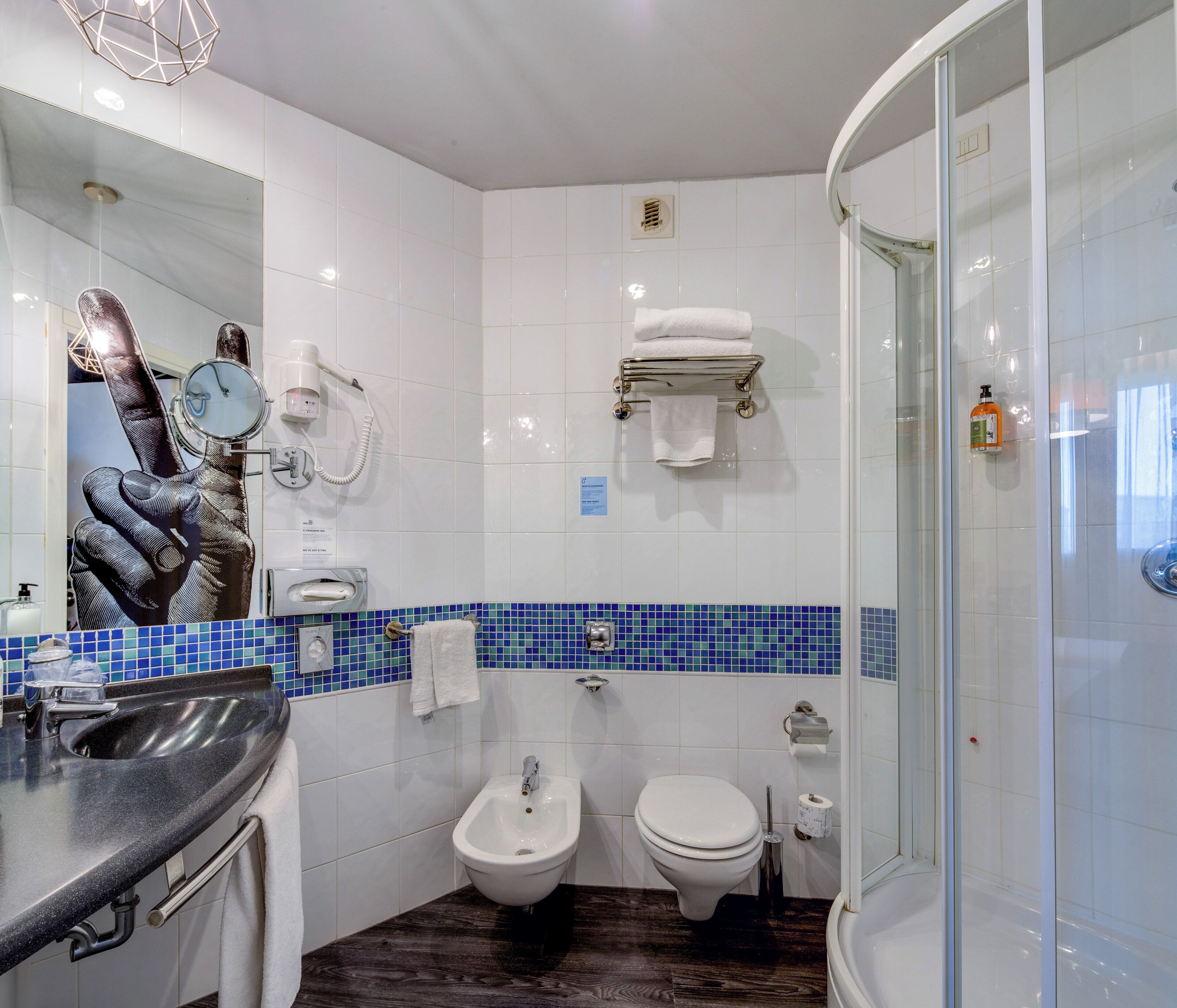 Egy modern fürőszoba bidével, WC-vel és üvegfalas zuhanyzóval.