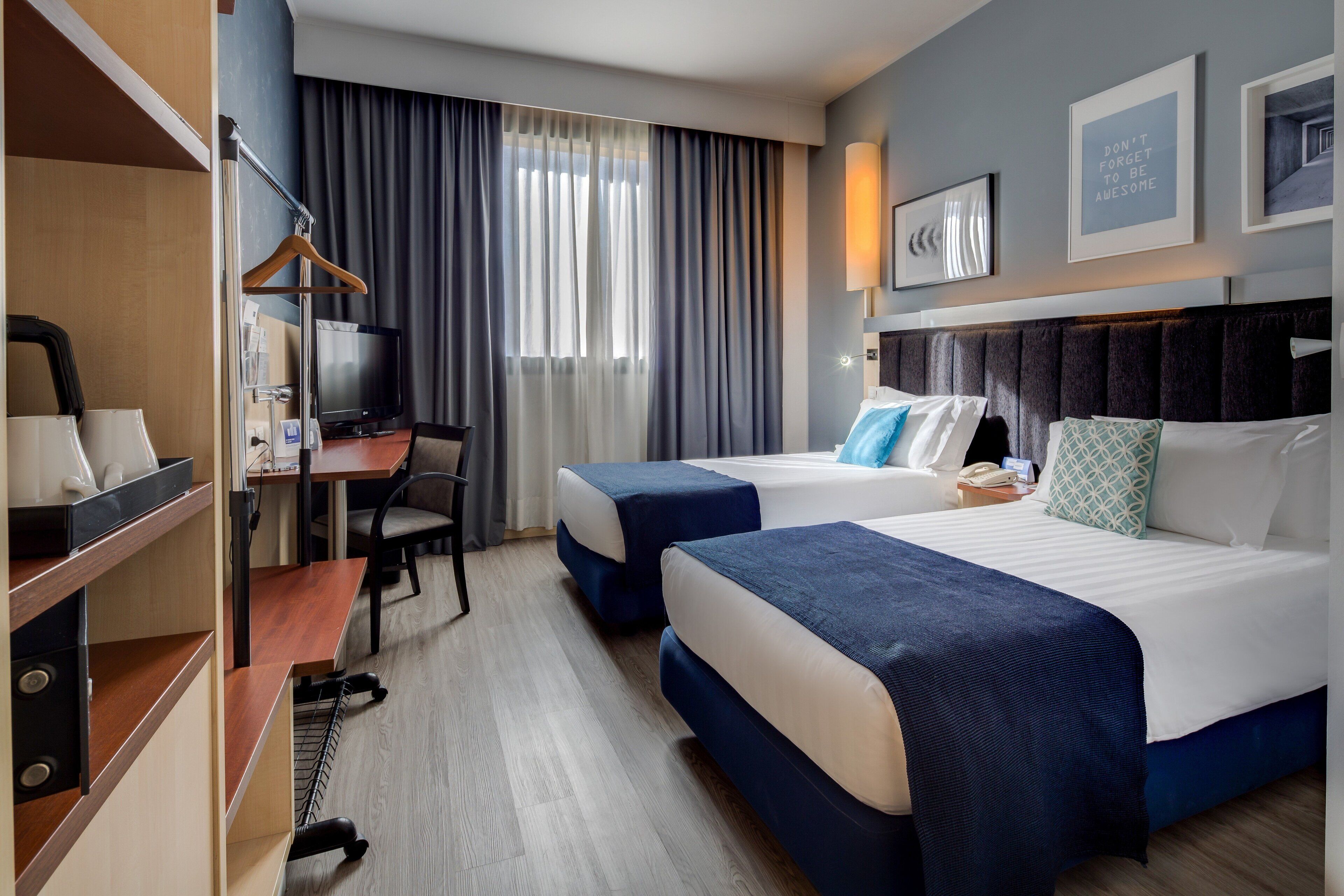 Ein Hotelzimmer mit zwei Betten, einem Schreibtisch, einem Sessel, einem Fernseher und einem Kleiderschrank.