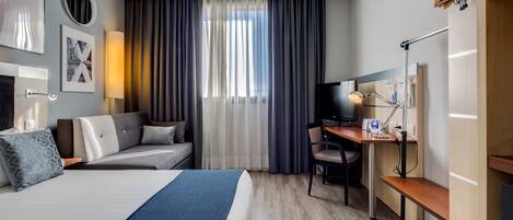 A hotel room with a large bed, a desk with a computer, a chair, and a TV.