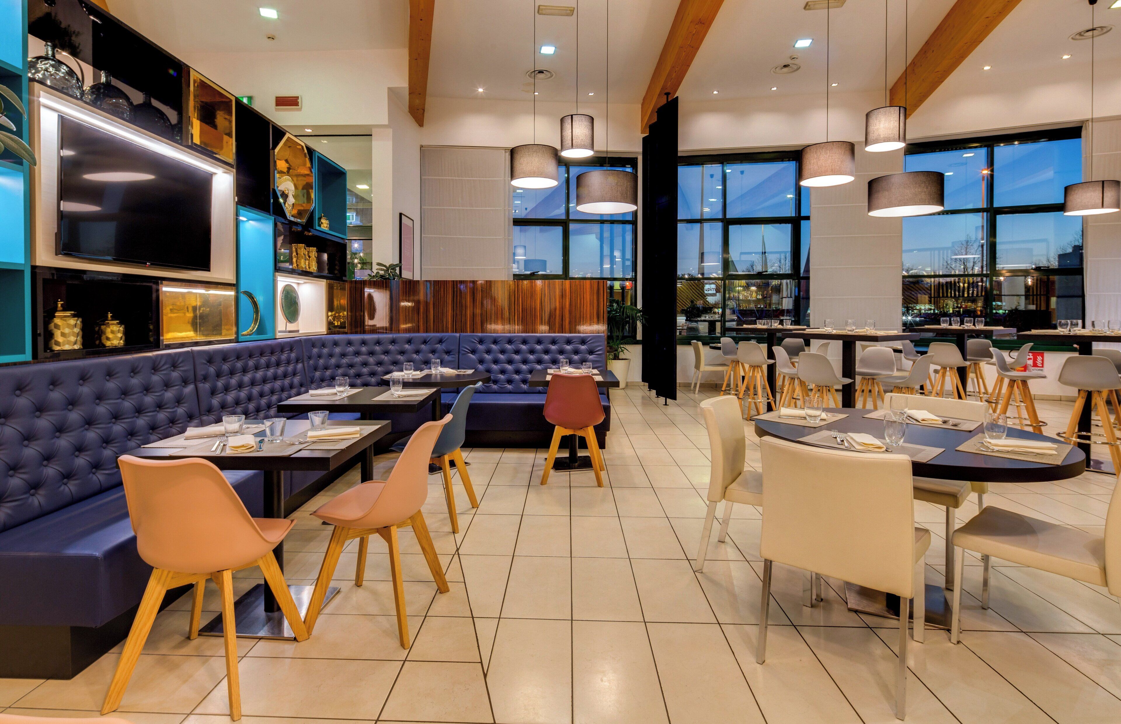 Un restaurant avec un coin salon doté de sièges rembourrés bleus, de tables et de chaises en bois.