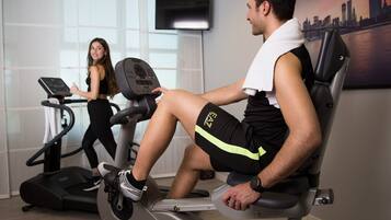 Une salle de sport équipée de matériel d’exercice, notamment des tapis de course et un vélo d’appartement, et dont un mur est décoré d’une fresque représentant un paysage urbain.