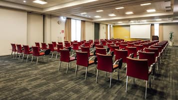 Ein Konferenzraum mit Reihen roter Stühle, einer Projektionsleinwand und einem Teppichboden.