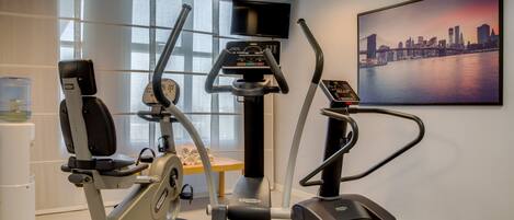 A fitness room with cardio machines, a water dispenser, and a cityscape painting.