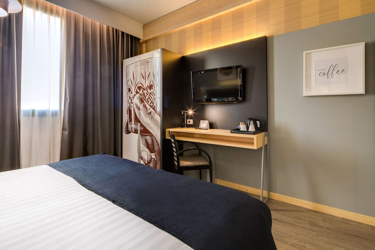 A hotel room with a bed, a desk with a chair, a TV, and a framed picture on the wall.