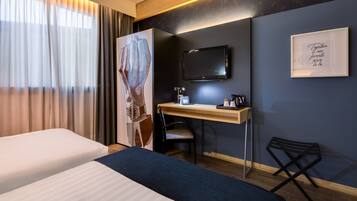Ein Hotelzimmer mit zwei Betten, einem Schreibtisch mit Stuhl, einem Fernseher und Bildern an der Wand.