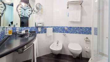 A modern bathroom with a black sink, a bidet, a toilet, and a glass-enclosed shower.