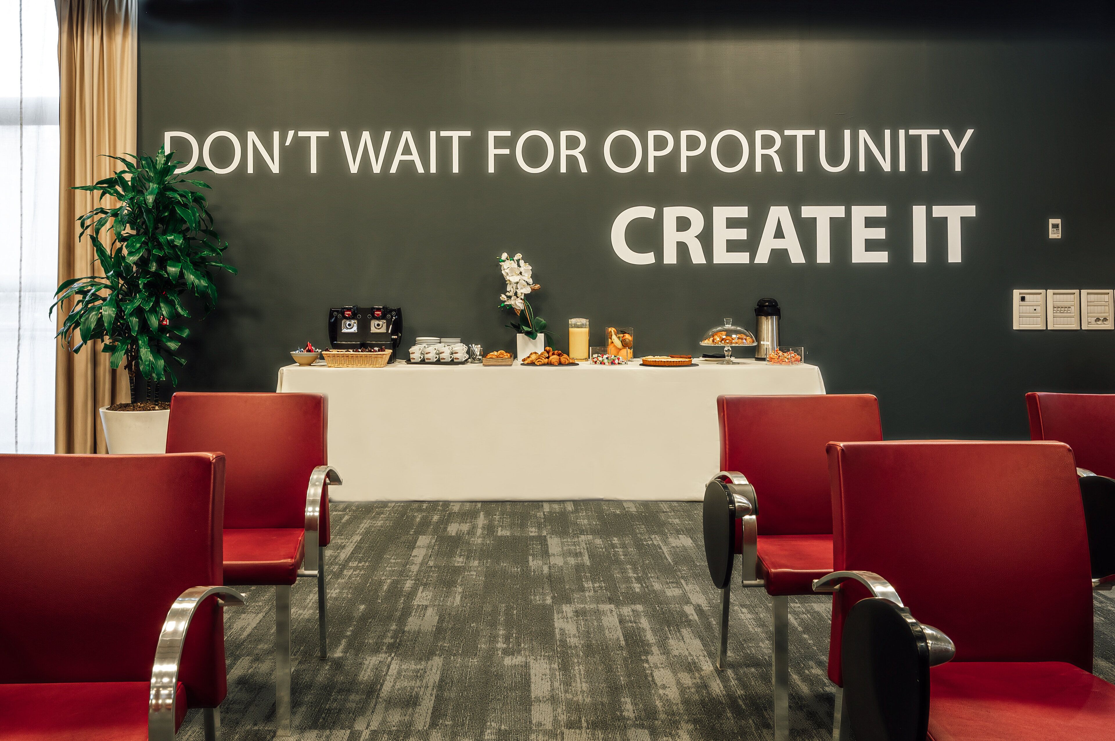 Un salón de conferencias con una cita inspiradora en la pared, una mesa de buffet con comida y sillas rojas.