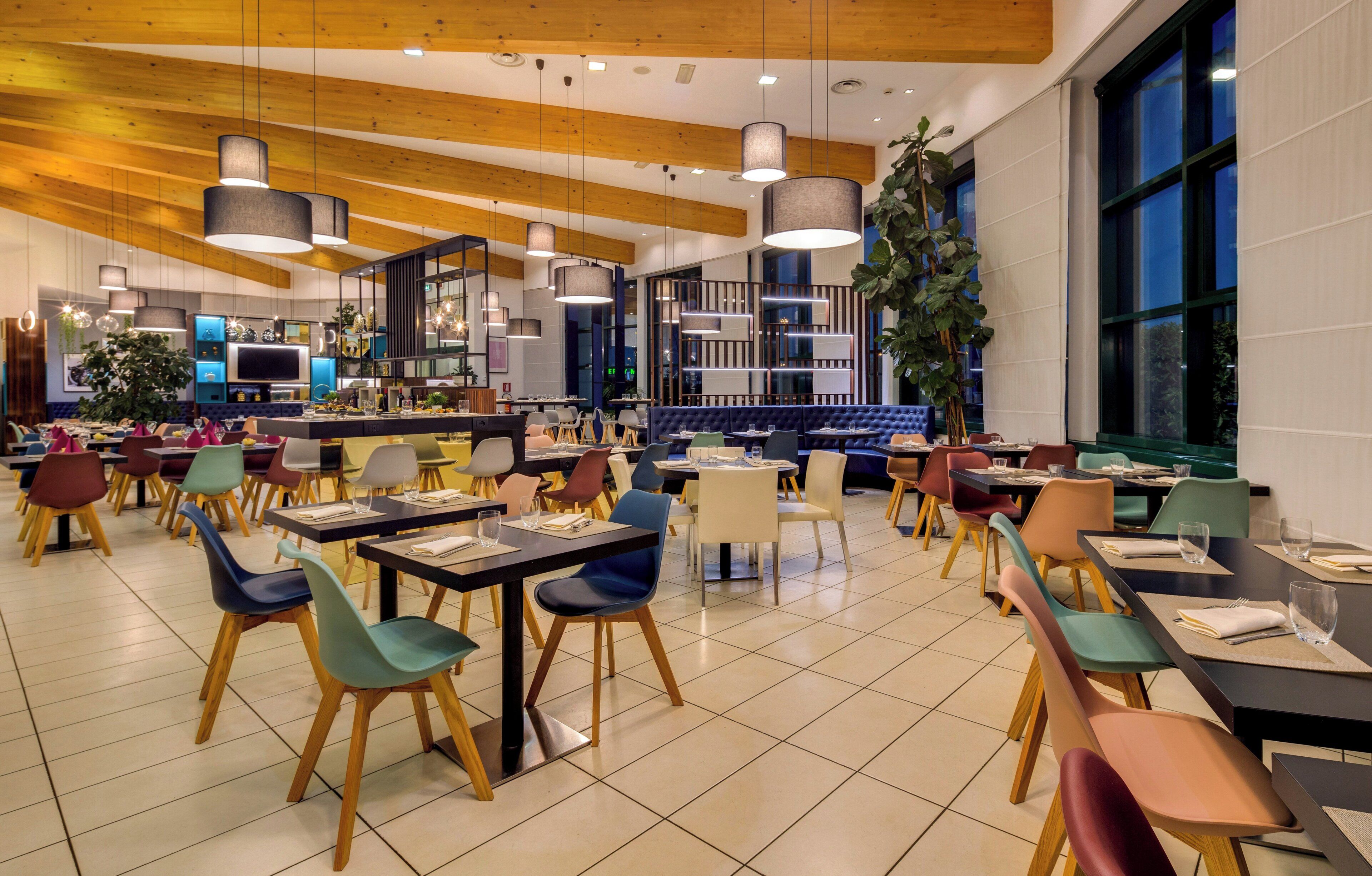 Un restaurante moderno con varias zonas de comedor, que incluyen un bar y una sala con una planta grande.