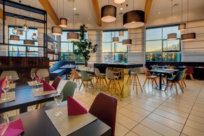 A restaurant with high tables, chairs, and hanging pendant lights. - Holiday Inn Bologna - Fiera by IHG (Bologna)