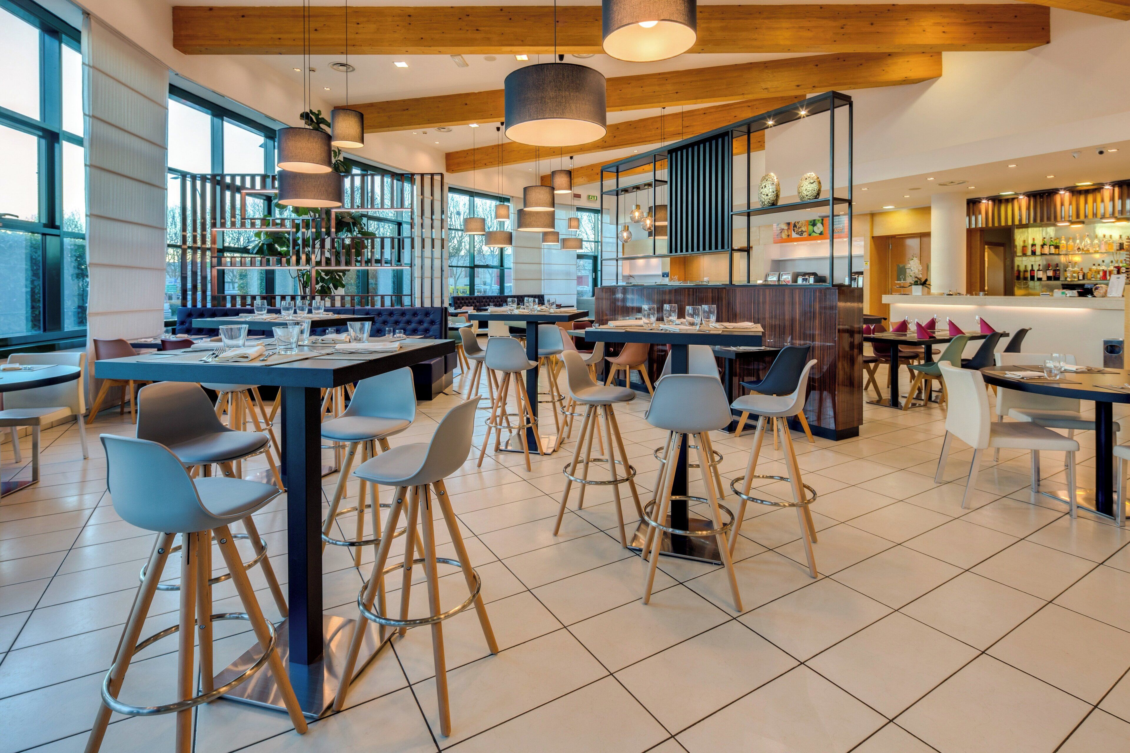 Un interior de restaurante moderno con techos altos, vigas de madera a la vista y una combinación de zonas de bar y comedor.
