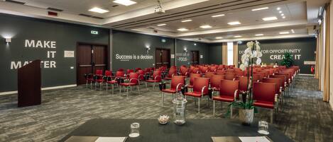 A conference room with rows of red chairs, a podium, and motivational wall quotes.