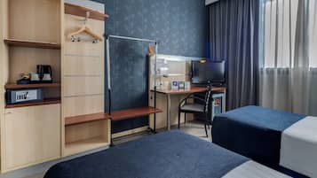 A hotel room with two beds, a desk with a computer, a TV, a wardrobe, and a small seating area.
