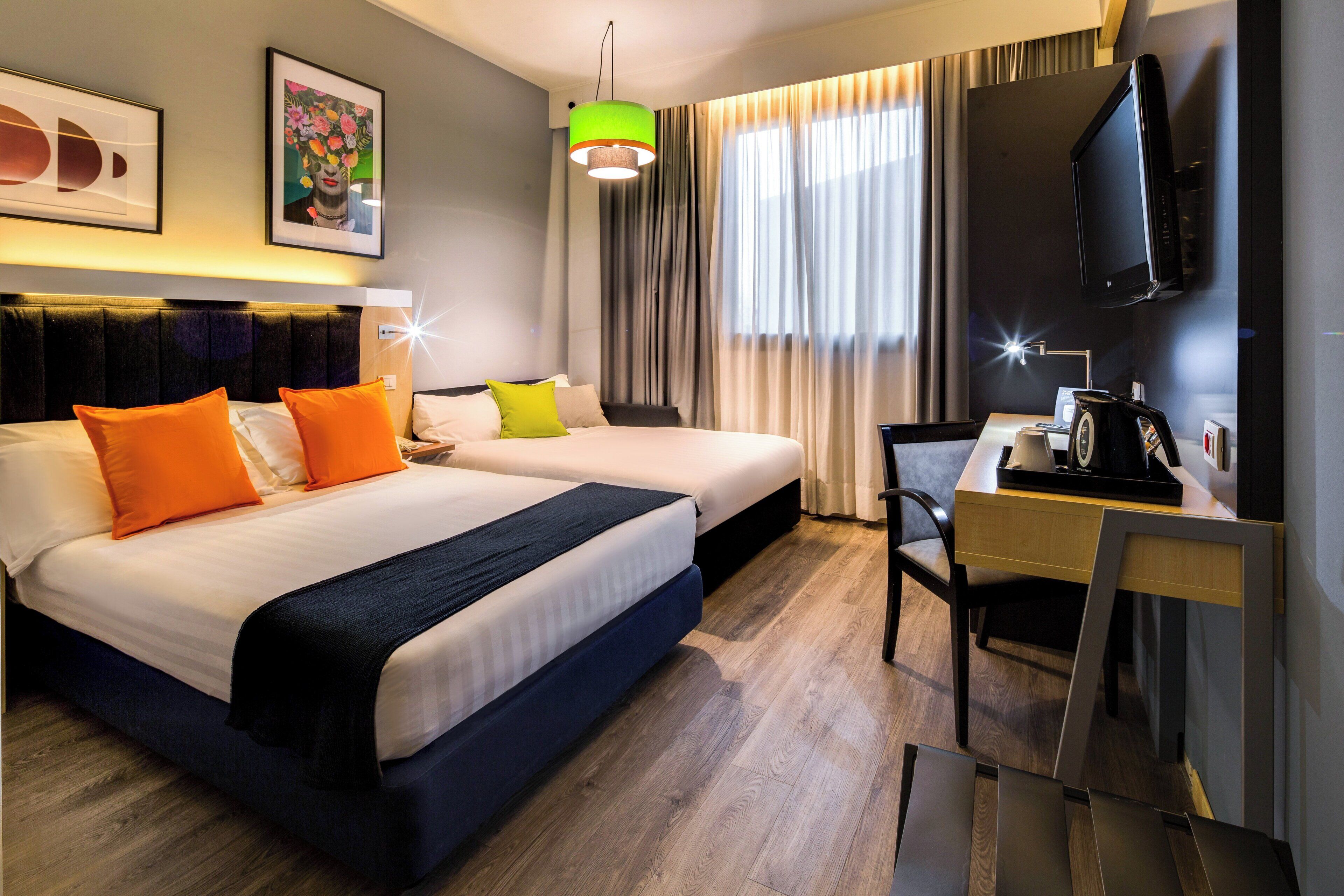 Une chambre d’hôtel avec deux lits, un bureau, une chaise, une télévision et une fenêtre avec des rideaux.
