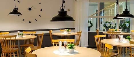 Un comedor con mesas redondas, sillas de madera, un reloj de pared y lámparas colgantes.