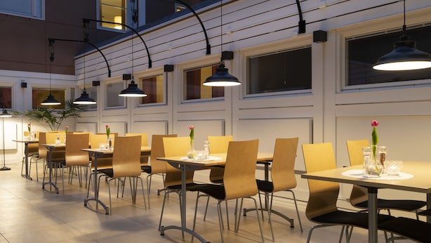 Un comedor con varias mesas y sillas, iluminación colgante y una planta en la esquina.
