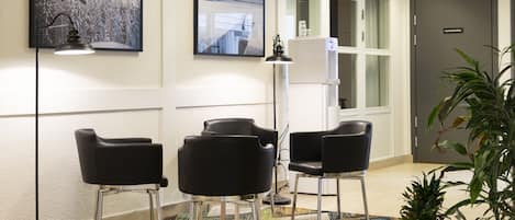 A conference room with three black chairs, a standing lamp, and two framed pictures on the wall.