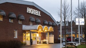 Un hotel con fachada de ladrillo, un letrero que dice "HOTEL VILJA" y un acceso cubierto con bancos.