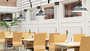 Un comedor moderno con mesas y sillas de madera, iluminación colgante y una planta en maceta.