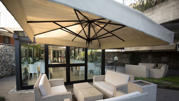 An outdoor seating area with wicker furniture and a large umbrella. - IH Hotels Milano Eur Trezzano sul Naviglio (Trezzano sul Naviglio)