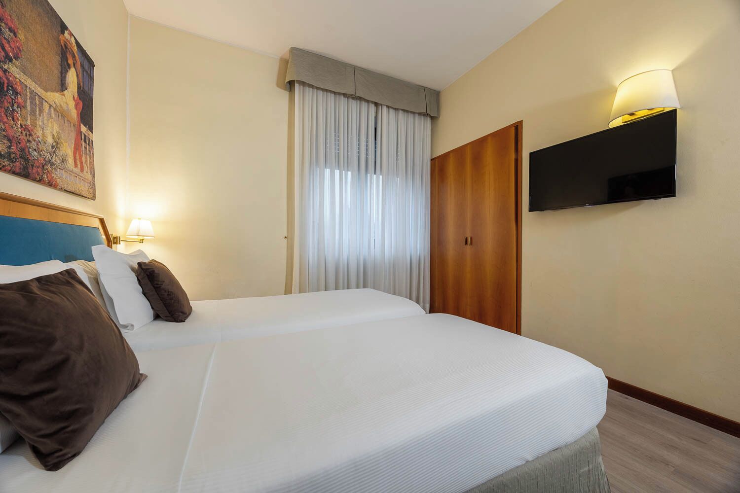Habitación de hotel con dos camas, un televisor montado en la pared y un cuadro colgado.