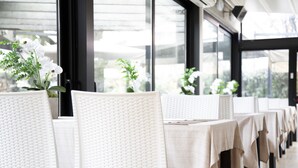 A row of tables with white tablecloths and wicker chairs, arranged in a dining area with large windows. - IH Hotels Milano Eur Trezzano sul Naviglio (Trezzano sul Naviglio)