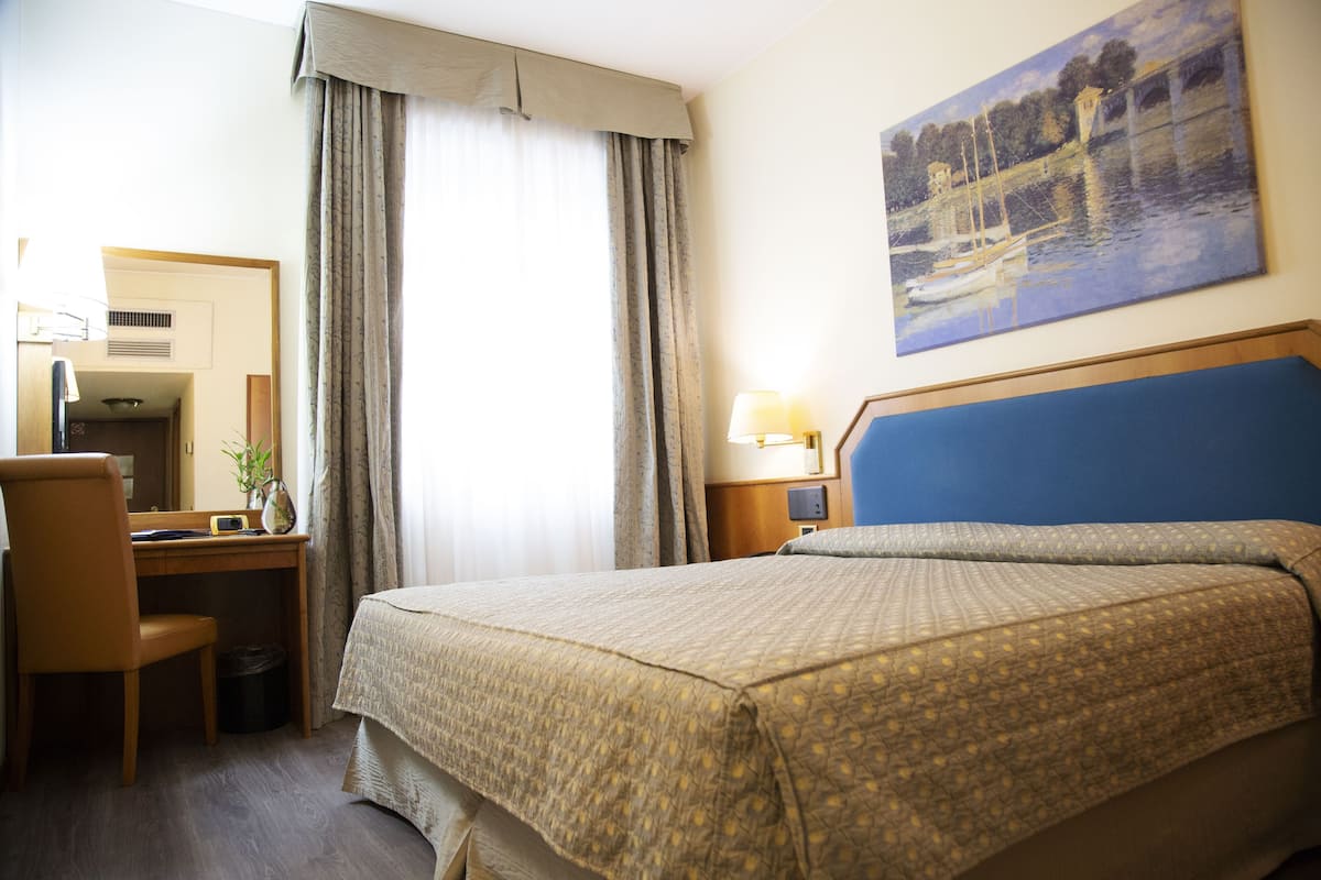 Habitación de hotel con cama, escritorio, silla y un cuadro en la pared.
