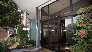 A building entrance with glass doors, a security camera, and a small garden with plants and flowers. - IH Hotels Milano Eur Trezzano sul Naviglio (Trezzano sul Naviglio)