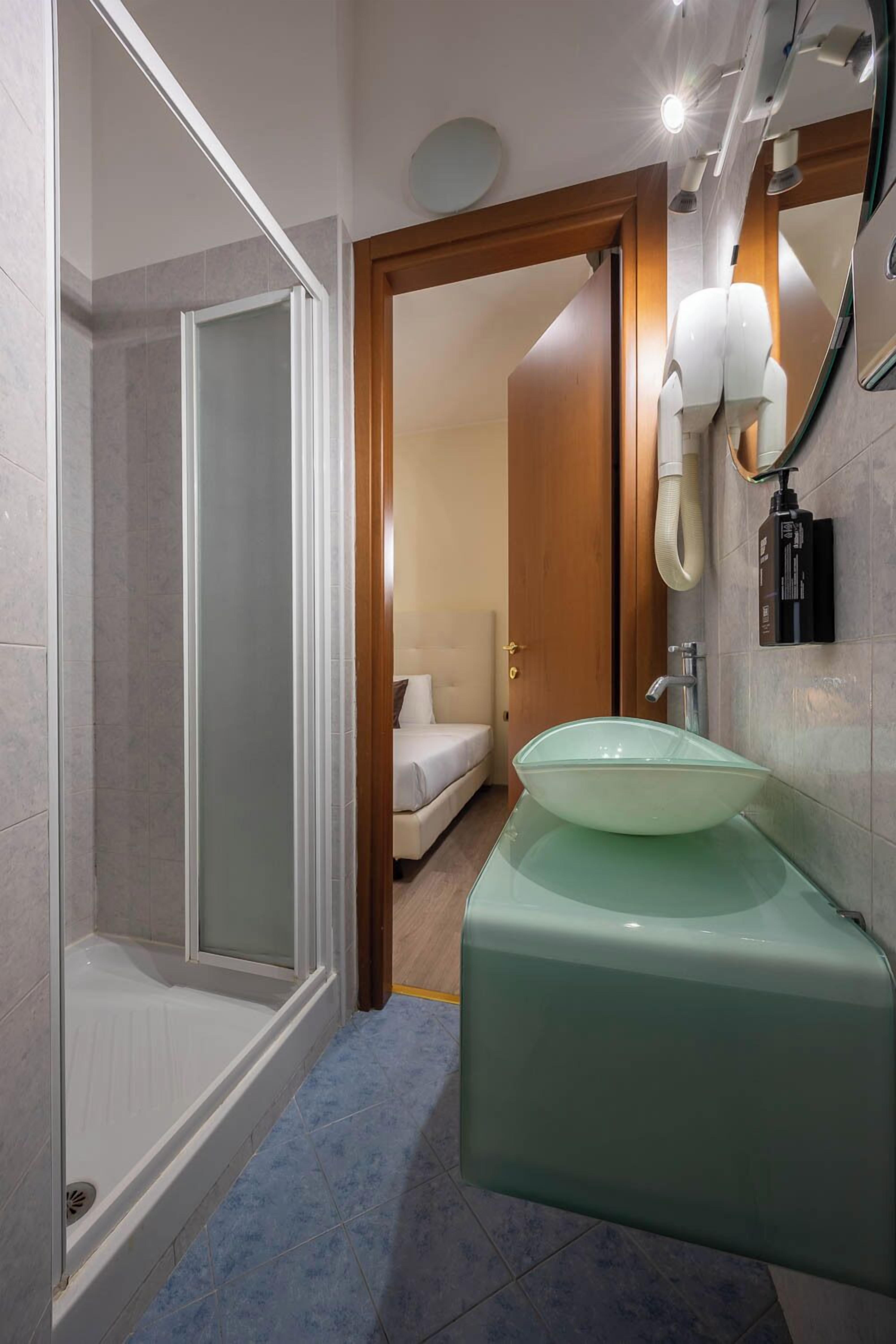Ein modernes Badezimmer mit Duschkabine aus Glas, einem grünen Waschbecken und einer weißen Toilette.
