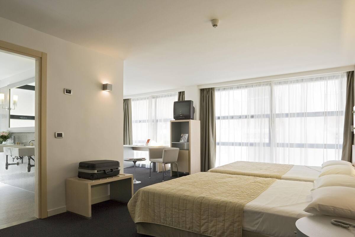 A hotel room with two beds, a desk, a chair, a television, and a window with curtains.