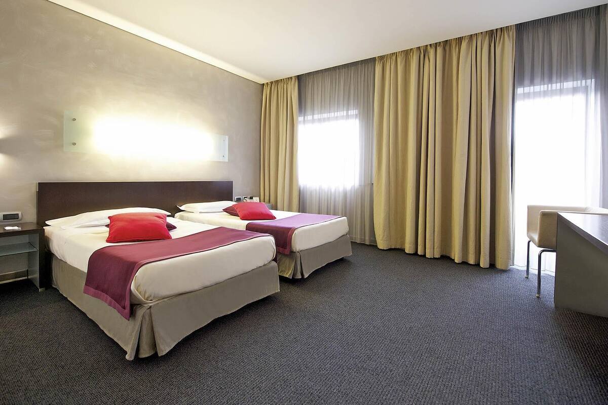 A hotel room with two beds, a desk, and a chair.