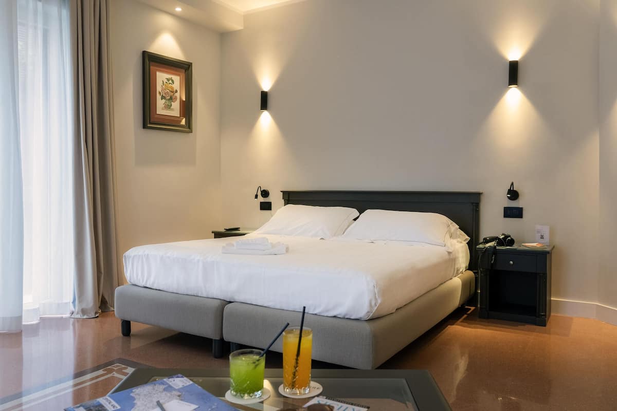 A hotel room with a large bed, bedside tables, a desk with a chair, and a window with curtains.