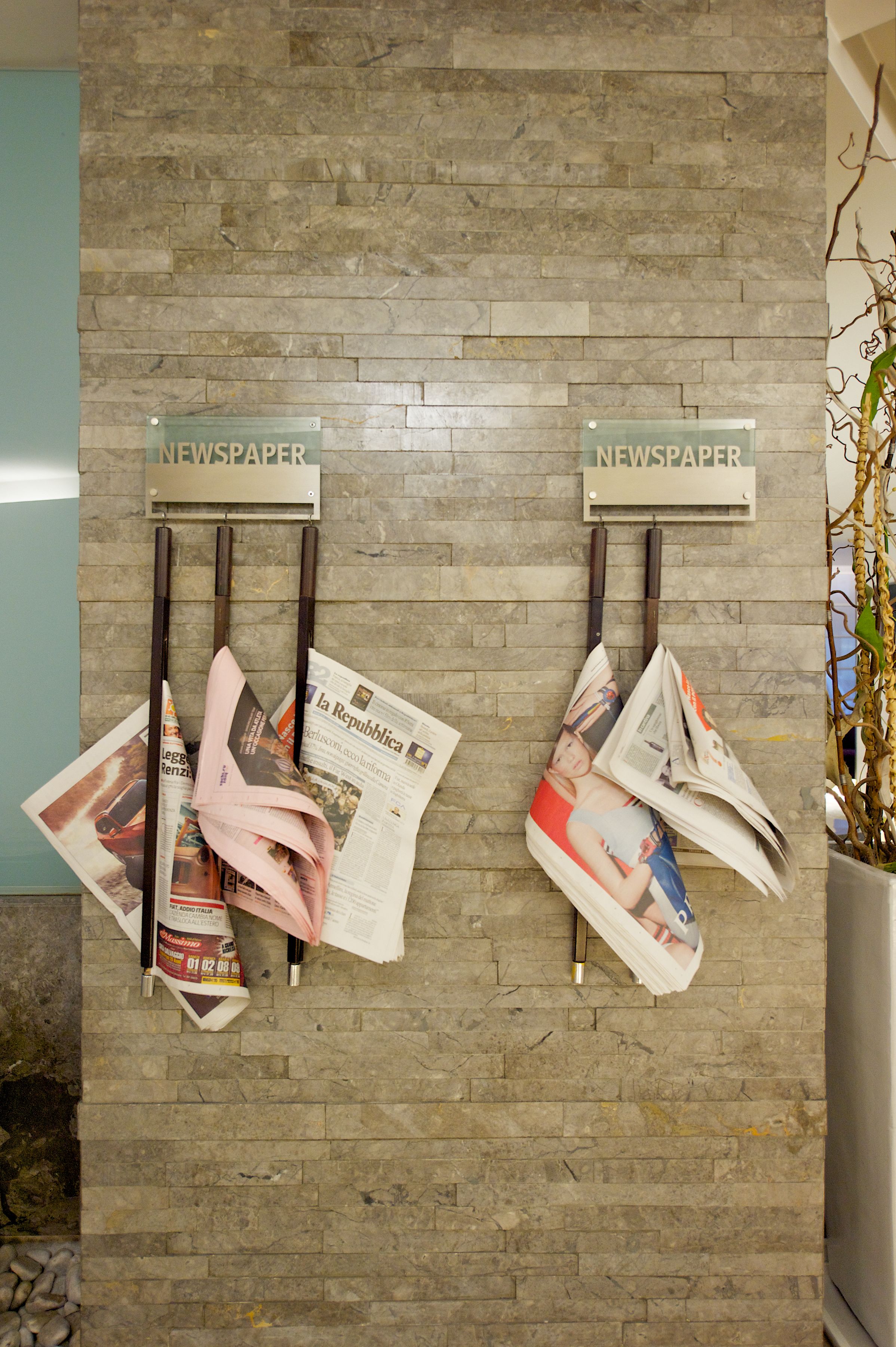 Two newspaper racks with folded newspapers on a brick wall.