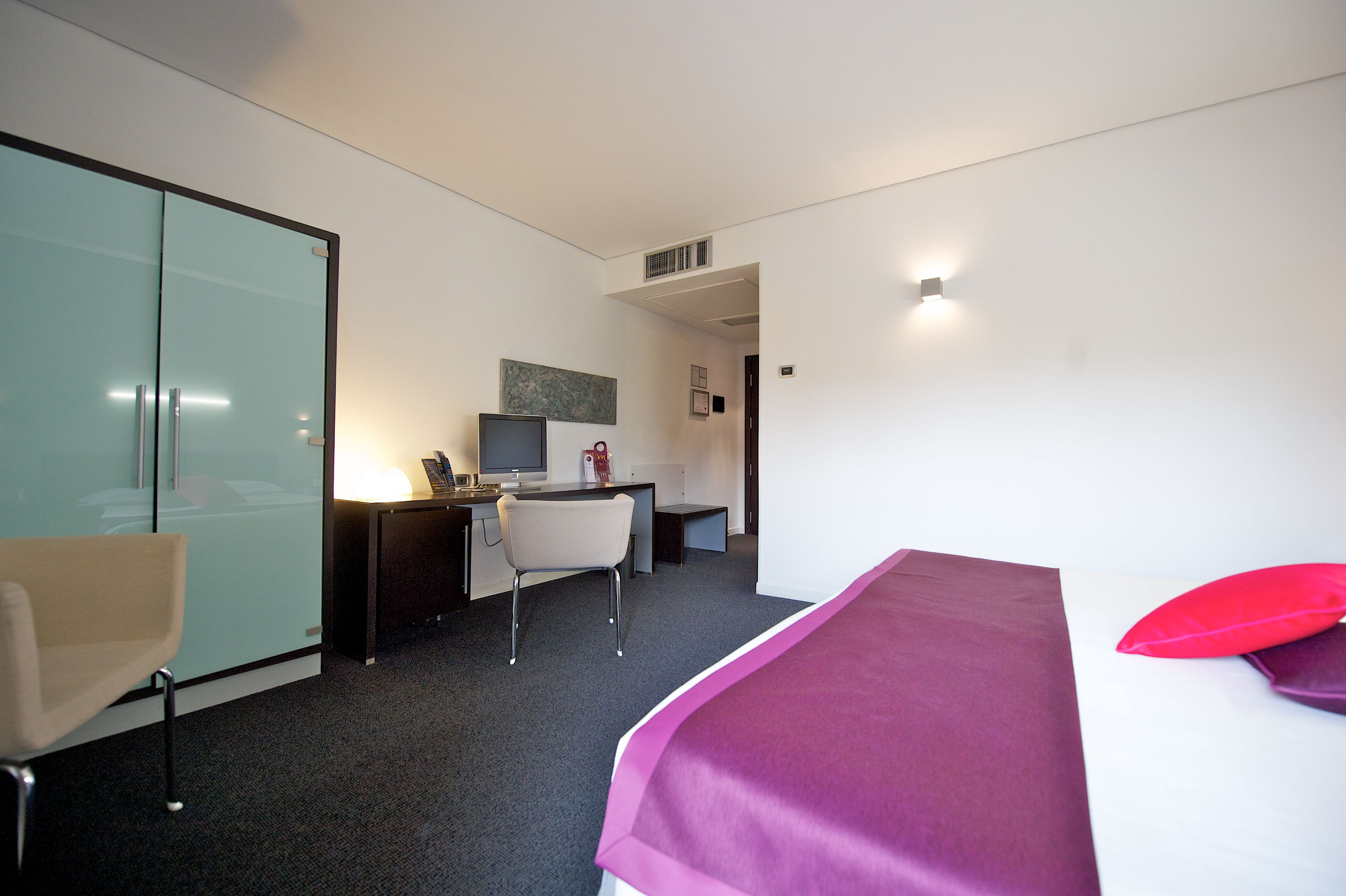 Une chambre d’hôtel comprenant un lit, un bureau, une chaise et une cloison en verre.