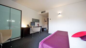 A hotel room with a bed, a desk, a chair, and a glass partition.