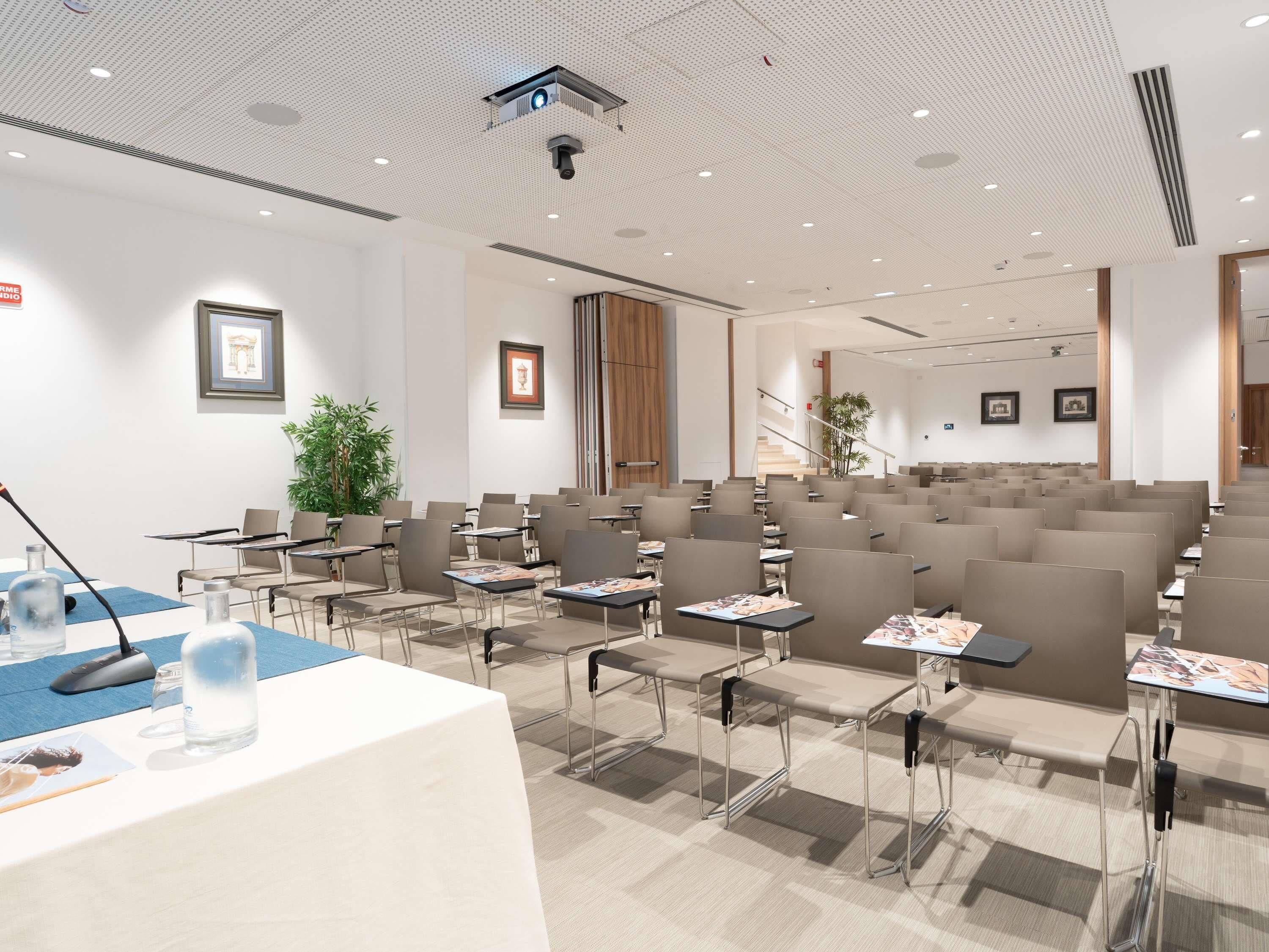 A conference room with rows of chairs, tables, a podium, and a projector.