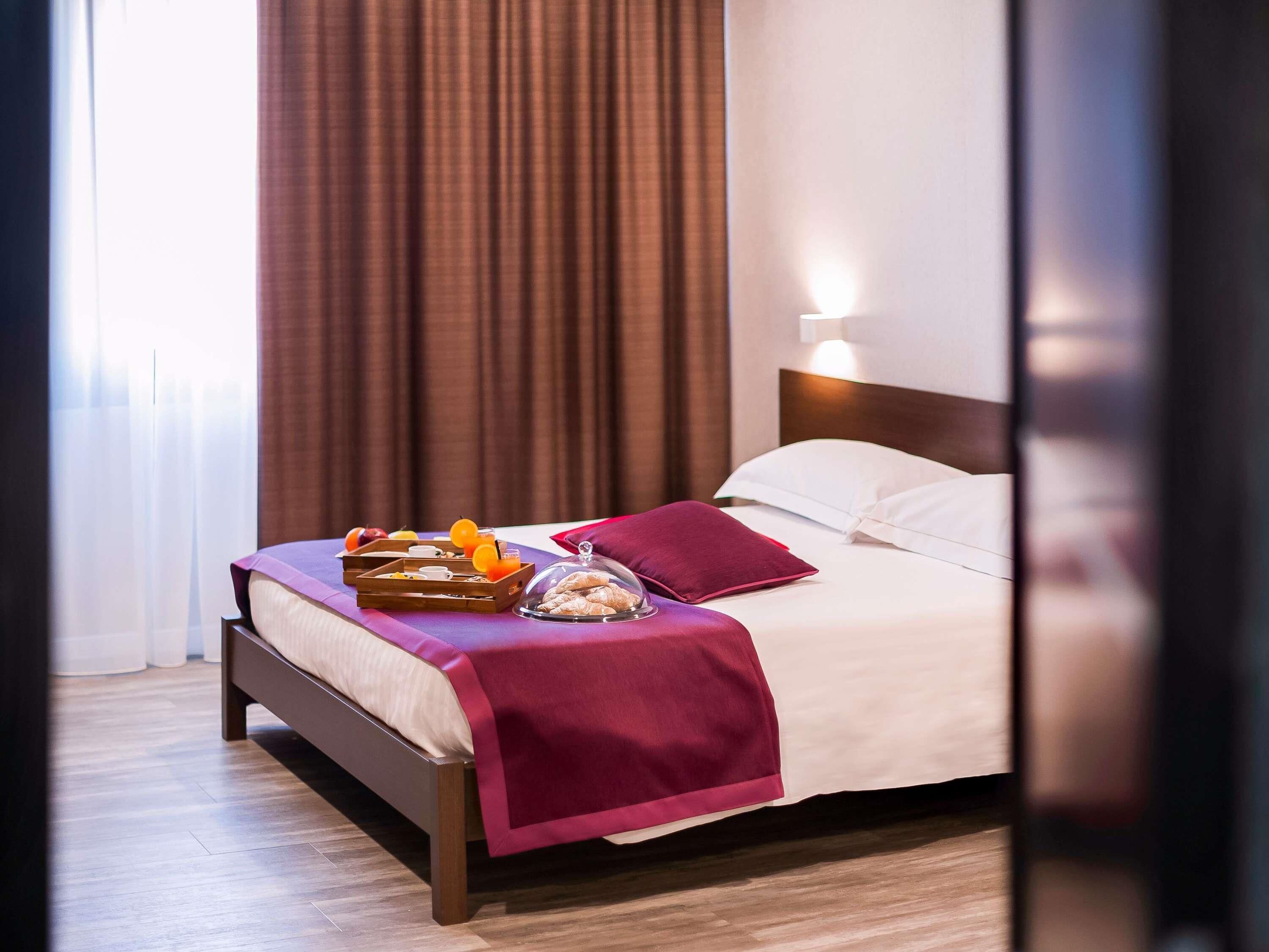 A hotel room with a bed, a nightstand, a lamp, and a window with curtains.